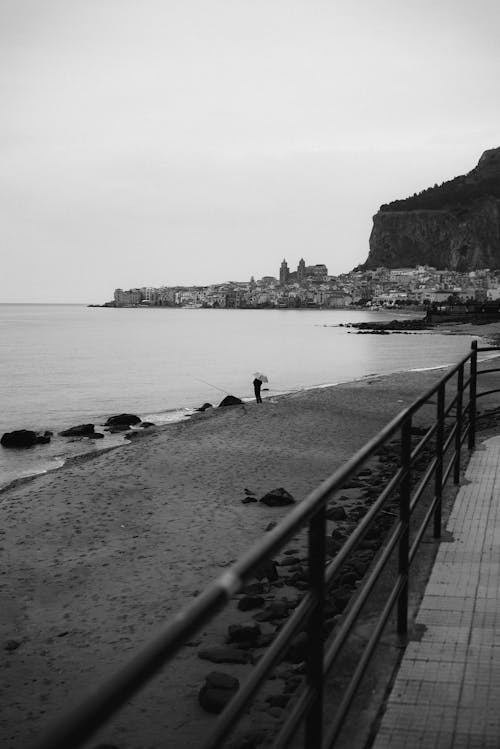 Black and white Photograph of a Shore and Town under a Rock in Background