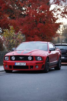 A sleek red Ford Mustang parked on a street with autumn trees in the background.