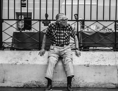 Old Man Sitting on Fencing Wall by Road
