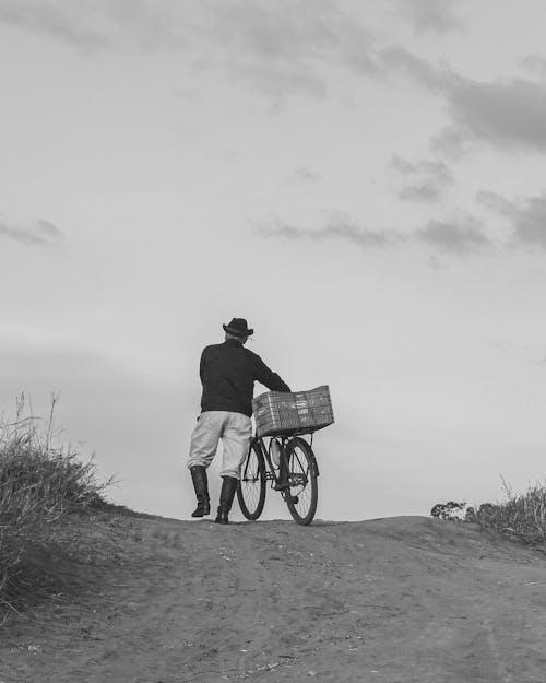 Senior Man in Hat Wheeling His Bike Uphill on Dirt Road