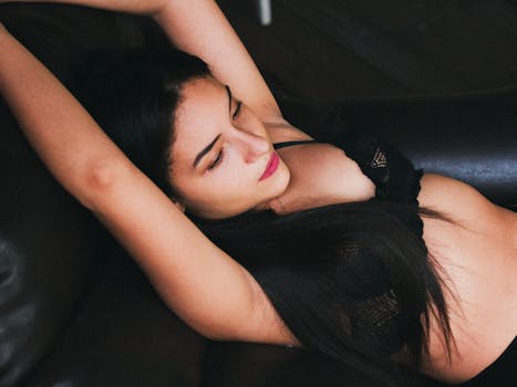 Portrait of a relaxed woman lying on a dark leather sofa in a black brassiere.