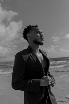 Black and white portrait of a man on the beach in Brazil wearing a blazer, showcasing a serene coastal ambiance.