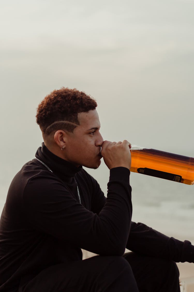 Man Sitting And Drinking Alcohol From Bottle