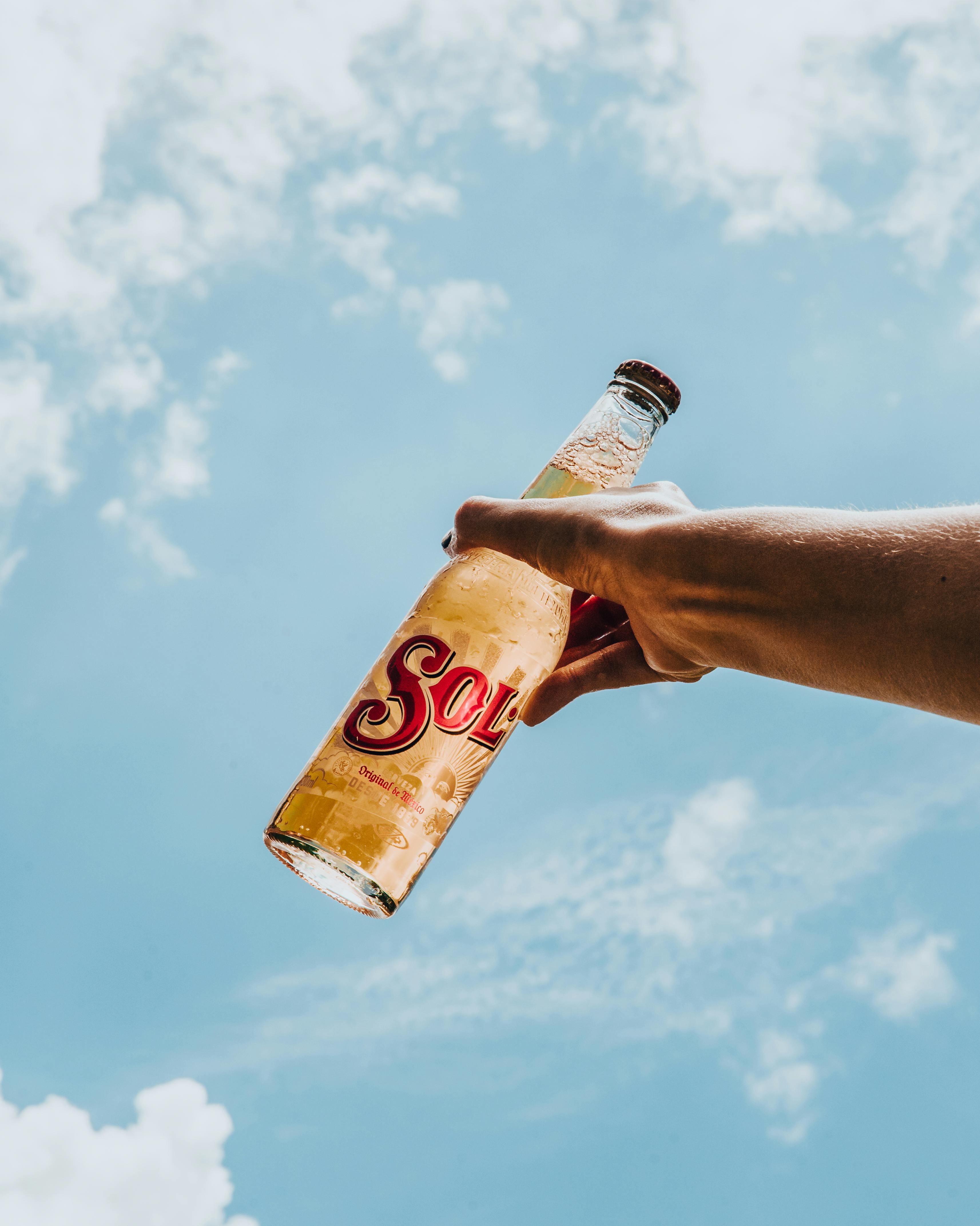 Hand holding a Sol beer bottle contrasting with the clear blue sky in São Paulo.