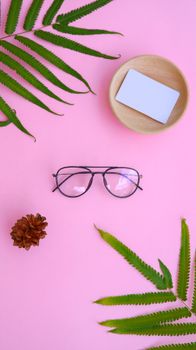 Elegant flat lay with glasses, fern leaves, and a wooden dish on pink background. Perfect for creative workspaces.