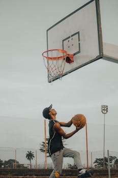 A young man skillfully jumping while aiming to score on an outdoor basketball court.