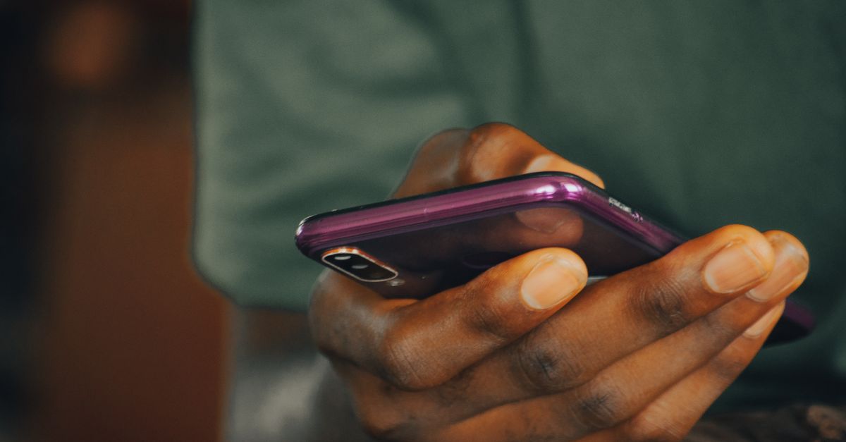 Uma foto em close de uma pessoa segurando um smartphone roxo indoors, focando em enviar mensagens ou navegar.