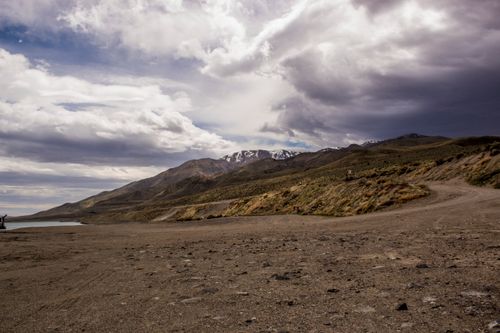 Free Majestic mountain landscape under a dramatic cloudy sky, featuring a winding dirt road. Stock Photo