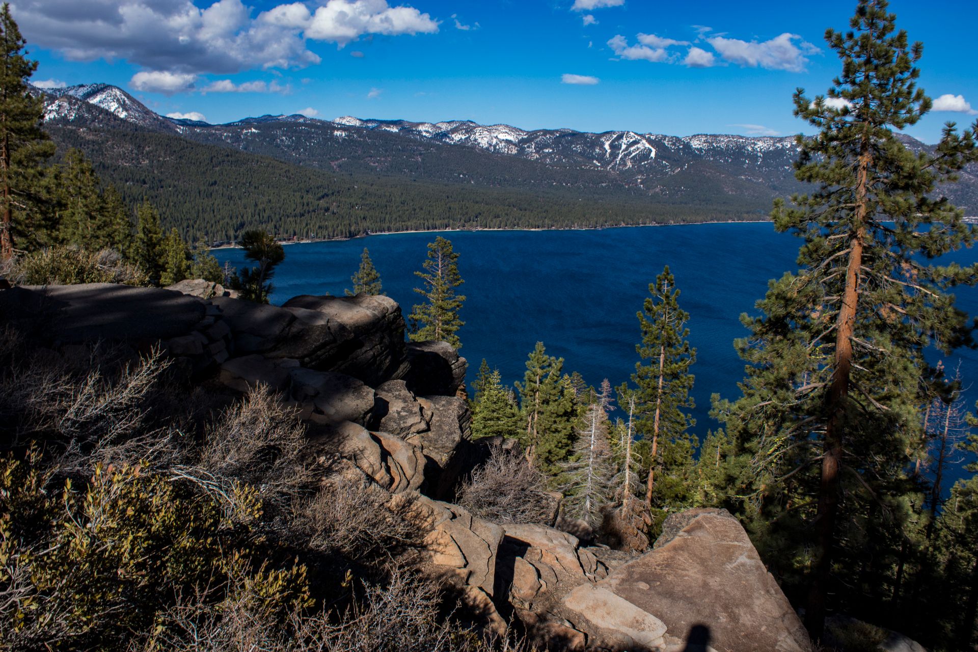 Breathtaking view of Lake Tahoe with surrounding forests and mountains, captured from a rocky cliff.