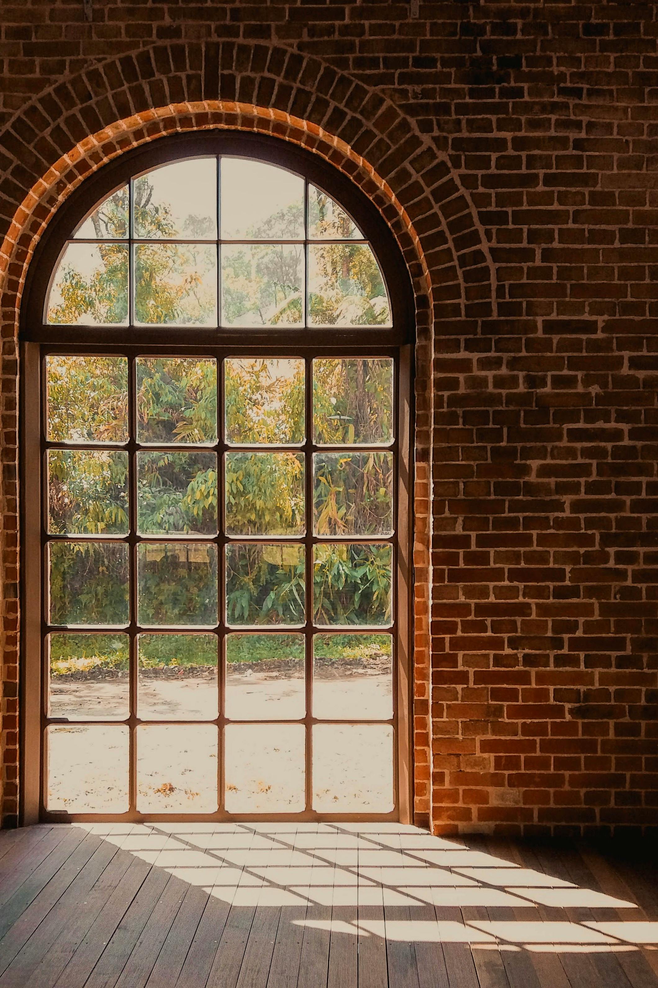 A sunlit arched window on a brick wall with shadow patterns creating a warm ambiance.