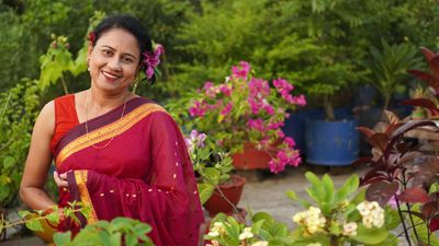 South Asian woman in a red saree stands in a vibrant garden, smiling with joy