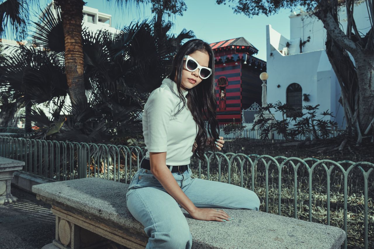 stylish woman in sunglasses sitting on a bench in a sunny park