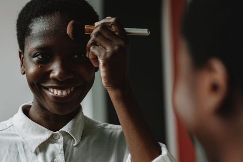 Free Close-up of a happy woman applying makeup, smiling at her reflection. Stock Photo