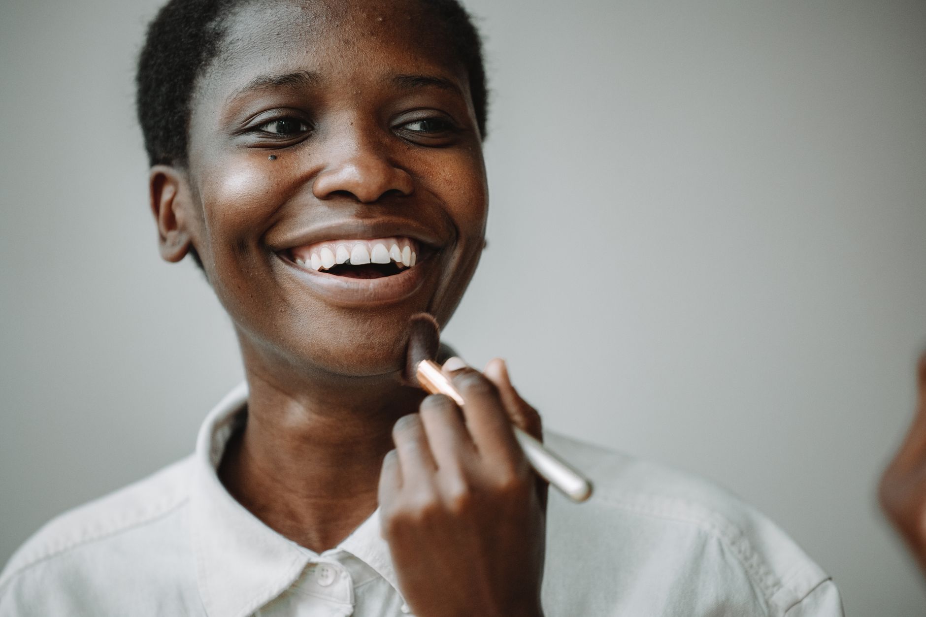 A joyful woman applies makeup using a brush, emphasizing a cheerful expression.