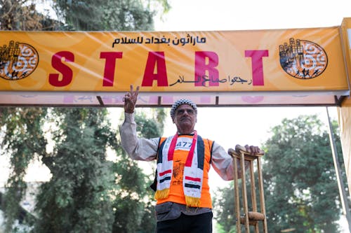 Man Wearing a Traditional Head Cover Standing at Race Start Banner with Crutches