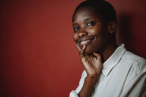 Free A woman wearing under eye masks and a button-down shirt smiles against a red backdrop. Stock Photo