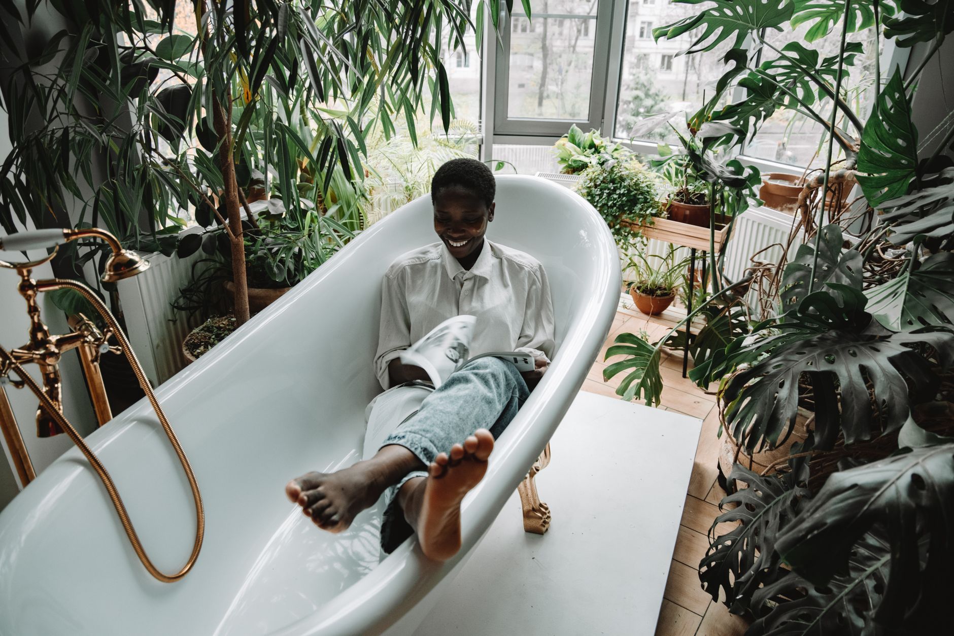 Content woman enjoying self-care in a bathtub, surrounded by lush indoor plants, embracing relaxation.