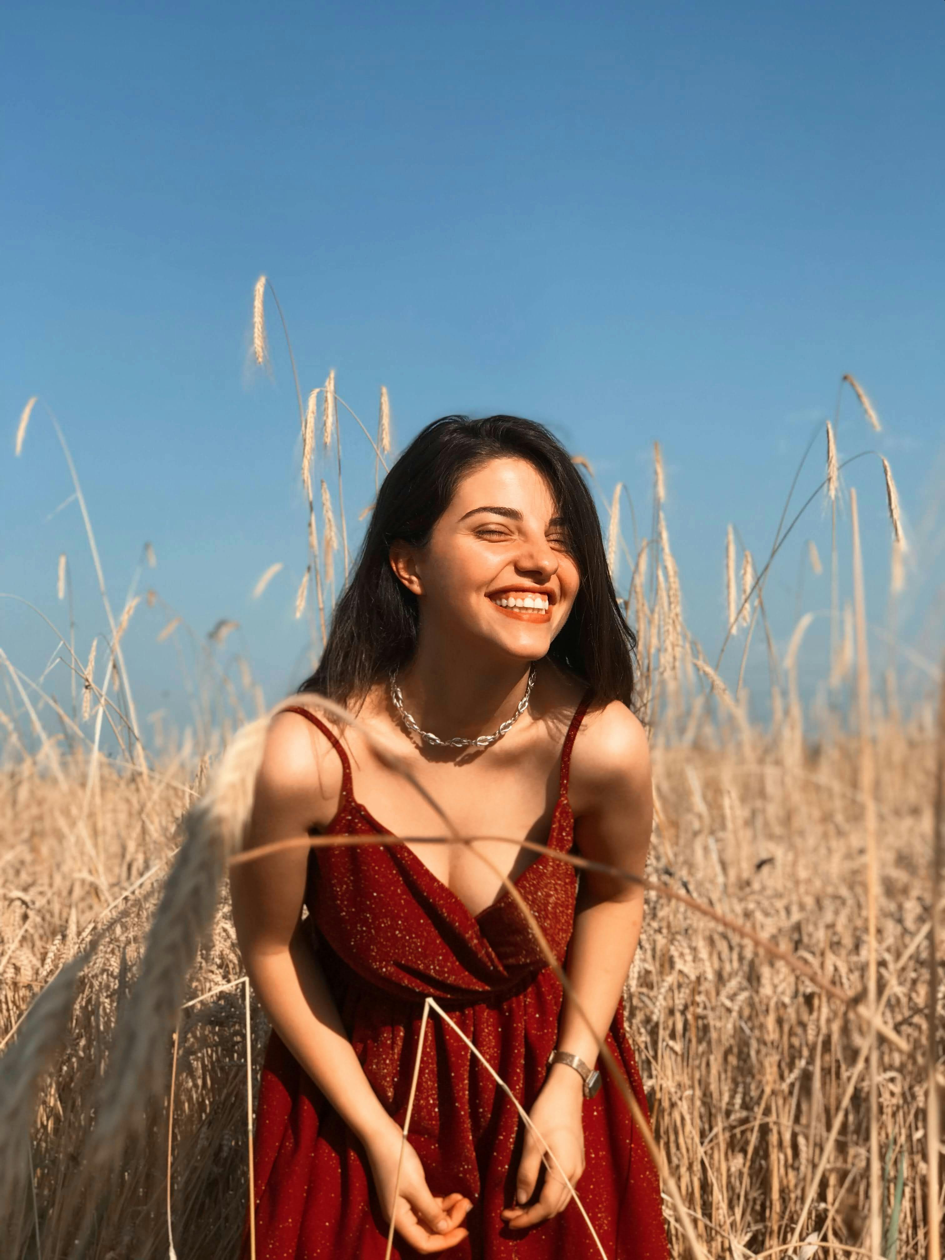 Young woman in a red dress beams in a sunny golden field, capturing summer's warmth.