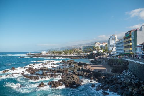 Free Rugged coastline of Puerto de la Cruz with vibrant buildings and blue sea. Stock Photo