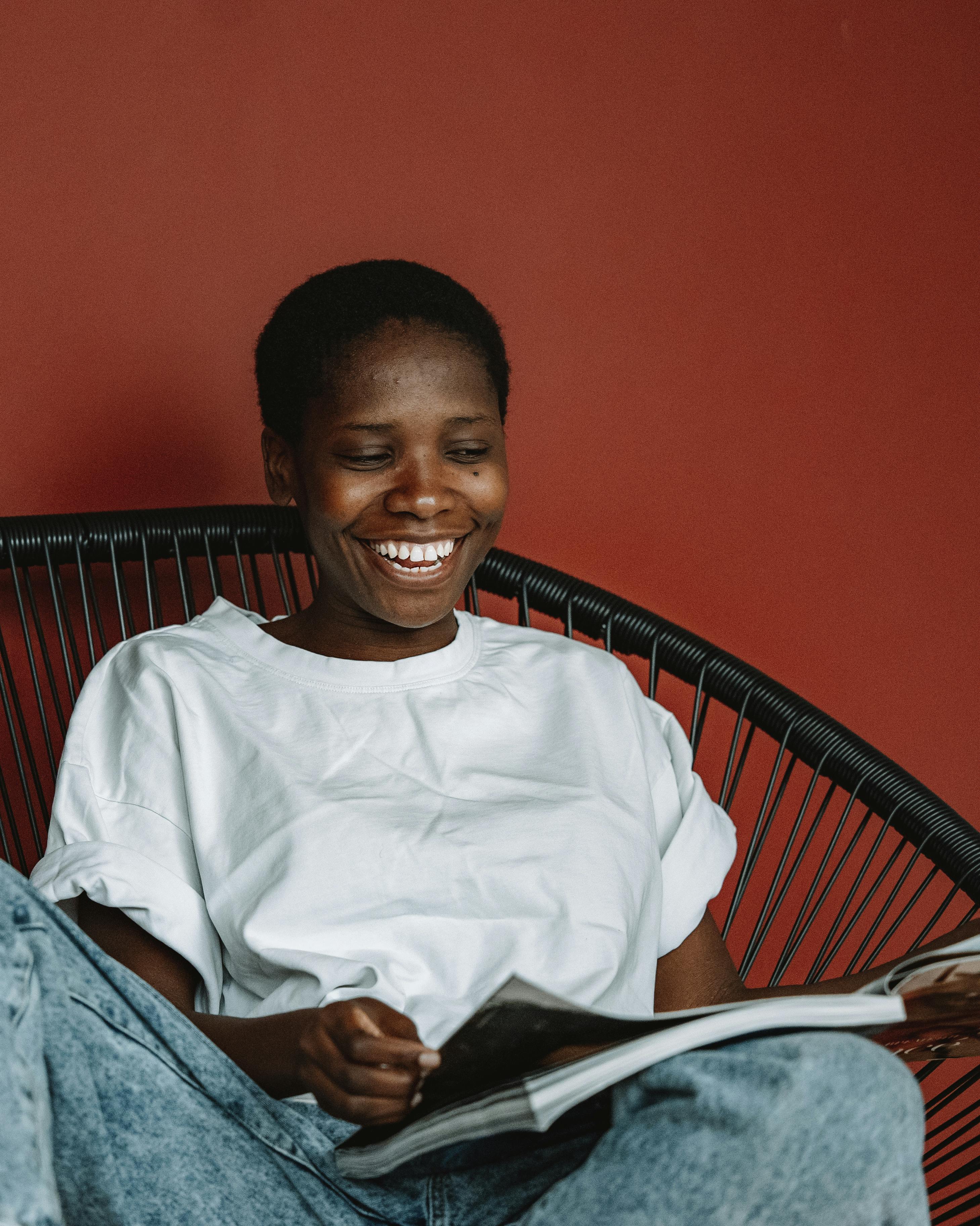 a woman in white crew neck t shirt sitting on black chair reading magazine