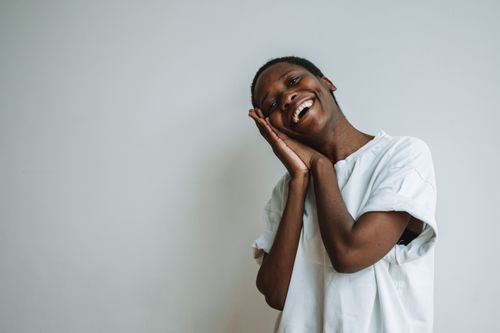 Free A joyful adult smiling with hands together in a gesture, wearing a white shirt against a plain background. Stock Photo