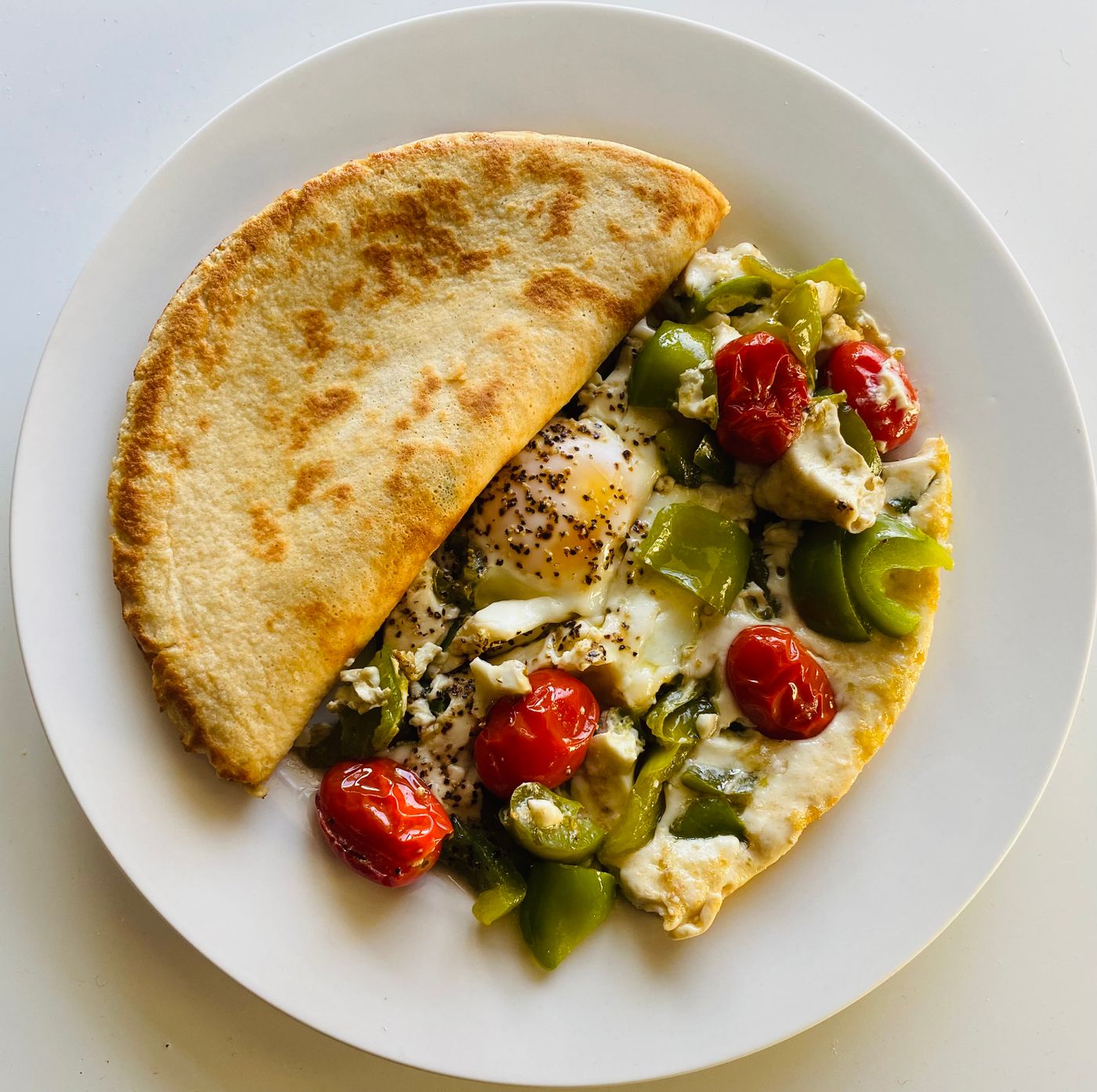 Delicious omelette topped with cherry tomatoes, bell peppers, and cheese, served on a white plate.