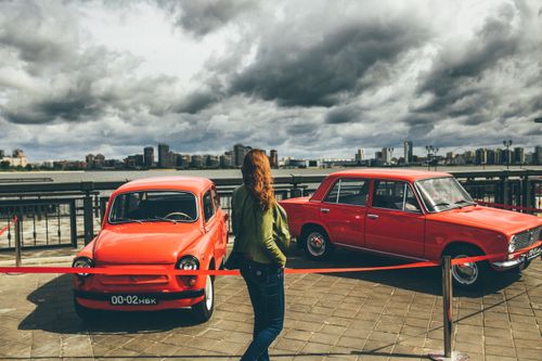 Free A woman observes classic red cars at an outdoor car exhibit under dramatic cloudy skies. Stock Photo