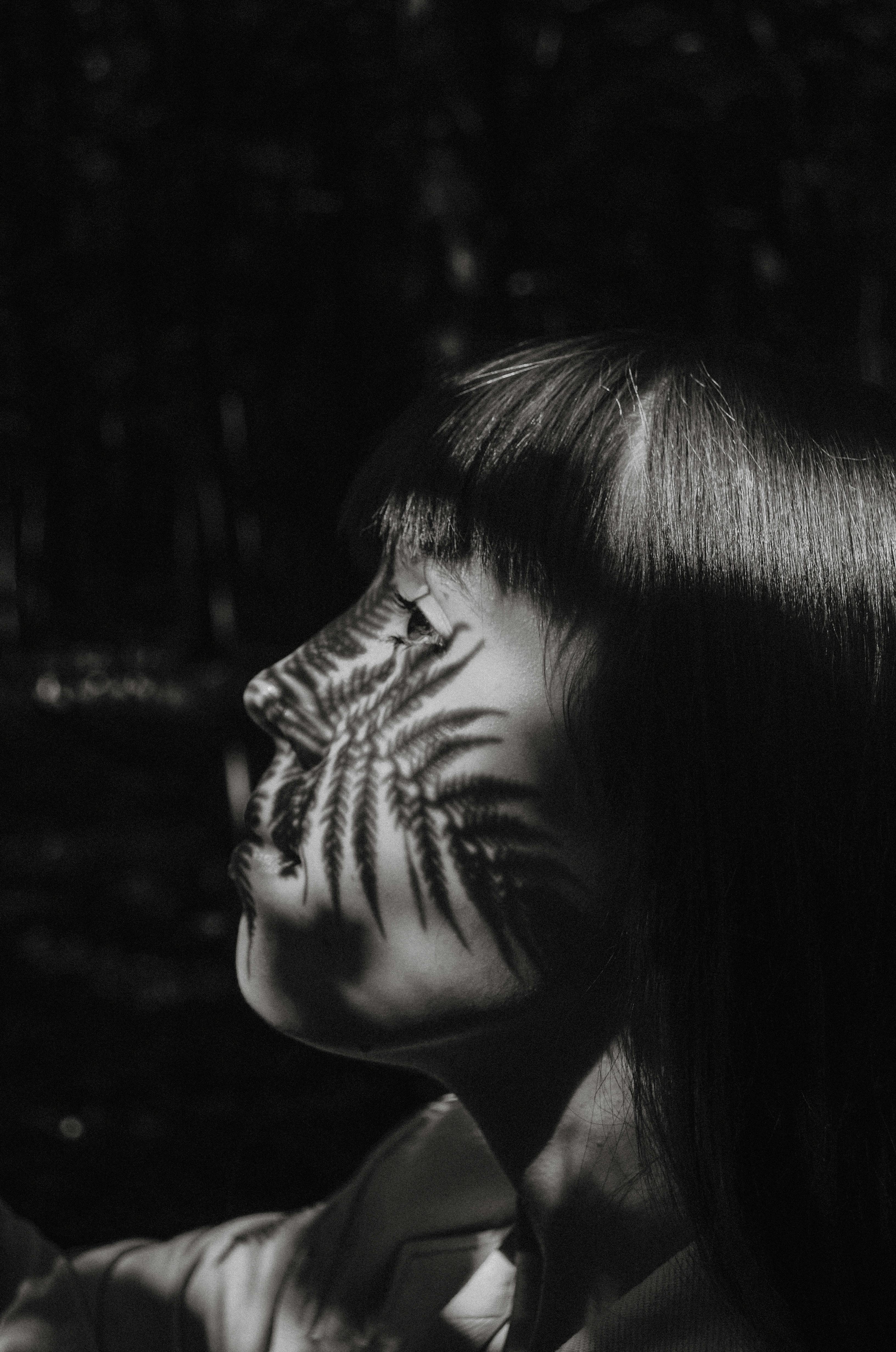 Black and white portrait of a woman with a fern shadow on her face, conveying a creative and abstract look.