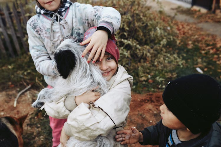 A Girl With Beanie Hugging A Black And White Dog