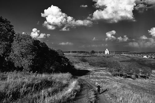 Grayscale Photo of Person Walking on Unpaved Road