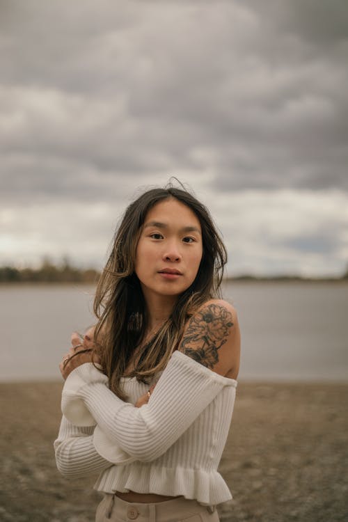 Woman in Sweater Standing on Shore Hugging Self