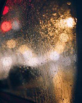 Blurry night city lights seen through a rain-soaked window, creating an atmospheric view.