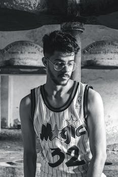 Black and white portrait of a young man wearing a Magic basketball jersey with eyeglasses.