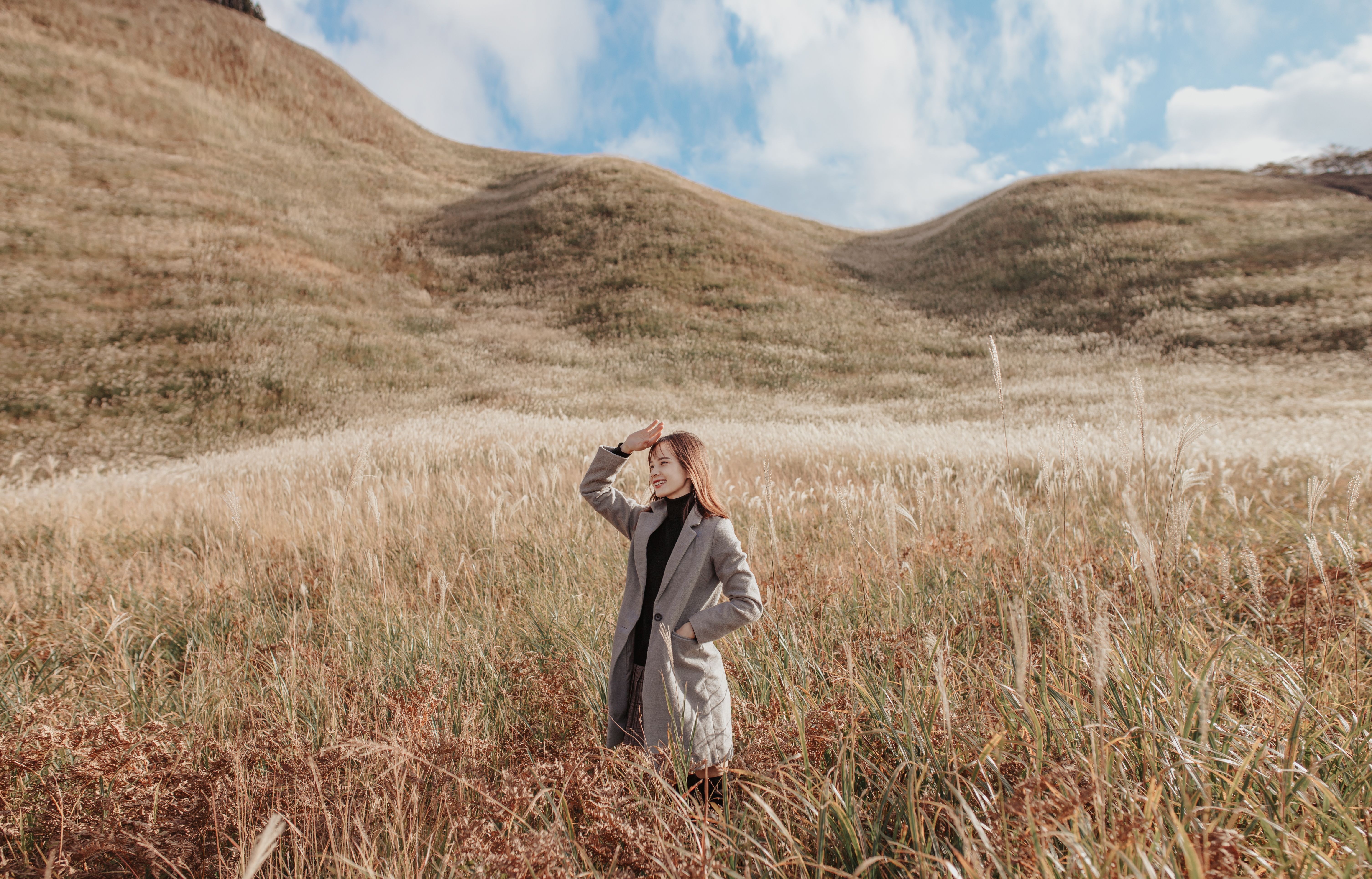 A young woman enjoys the serene beauty of a hilly grassland under a bright, sunny sky.