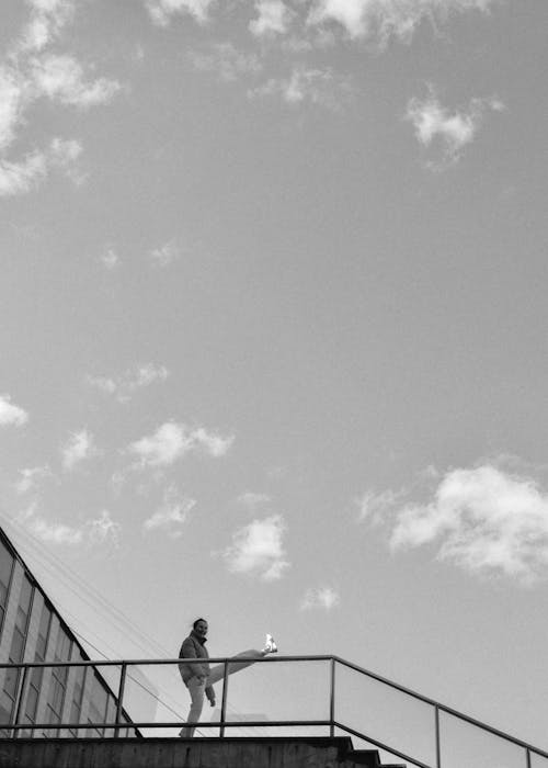 Grayscale Photo of Man Standing Beside the Railings