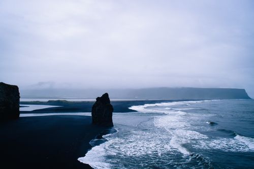 Free Stunning view of Iceland's black sand beach with rugged coastline and crashing waves. Stock Photo