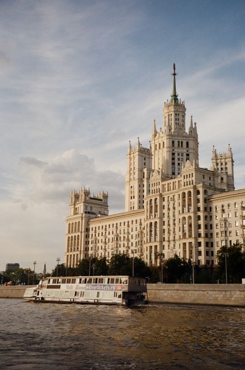 Free Stalinist skyscraper behind a boat on the Moskva River, showcasing Moscow's iconic architecture. Stock Photo