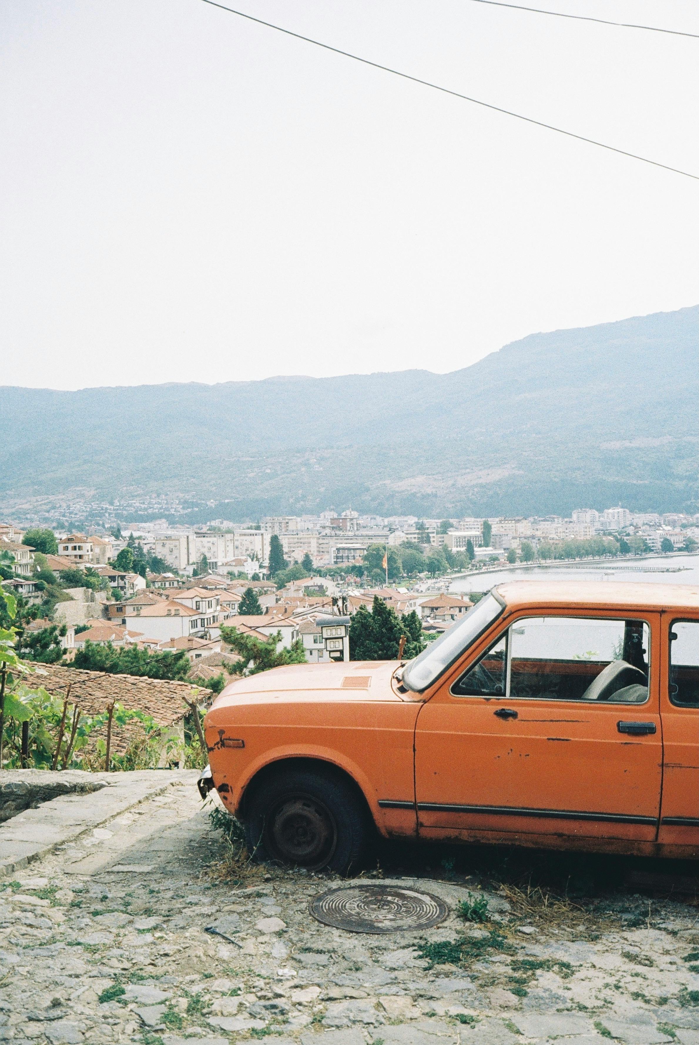 Explore Ohrid's beauty with a scenic view of an old car overlooking the city.