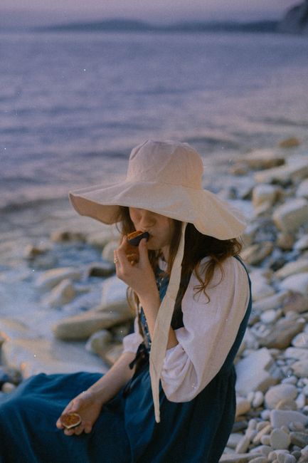 A woman in a sun hat sits by the rocky seaside in Gelendzhik, Russia, savoring the tranquility.