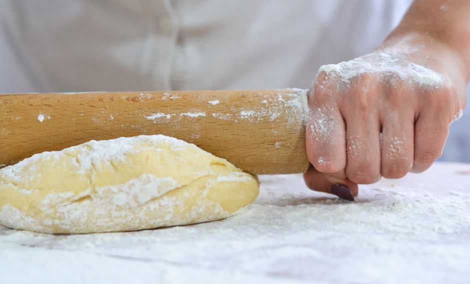 A hand rolling dough with a wooden rolling pin on a floured surface.