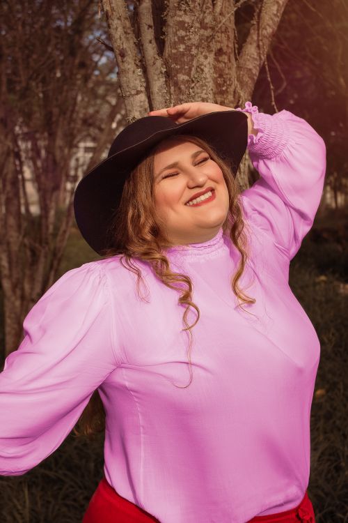 Free Joyful woman in a stylish pink blouse and black hat, enjoying a sunny day outdoors. Stock Photo