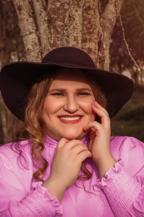 Free Portrait of a cheerful woman wearing a stylish black hat and pink top, posing happily outdoors. Stock Photo