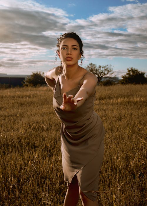 Woman in Brown Spaghetti Strap Dress Standing on Brown Grass Field