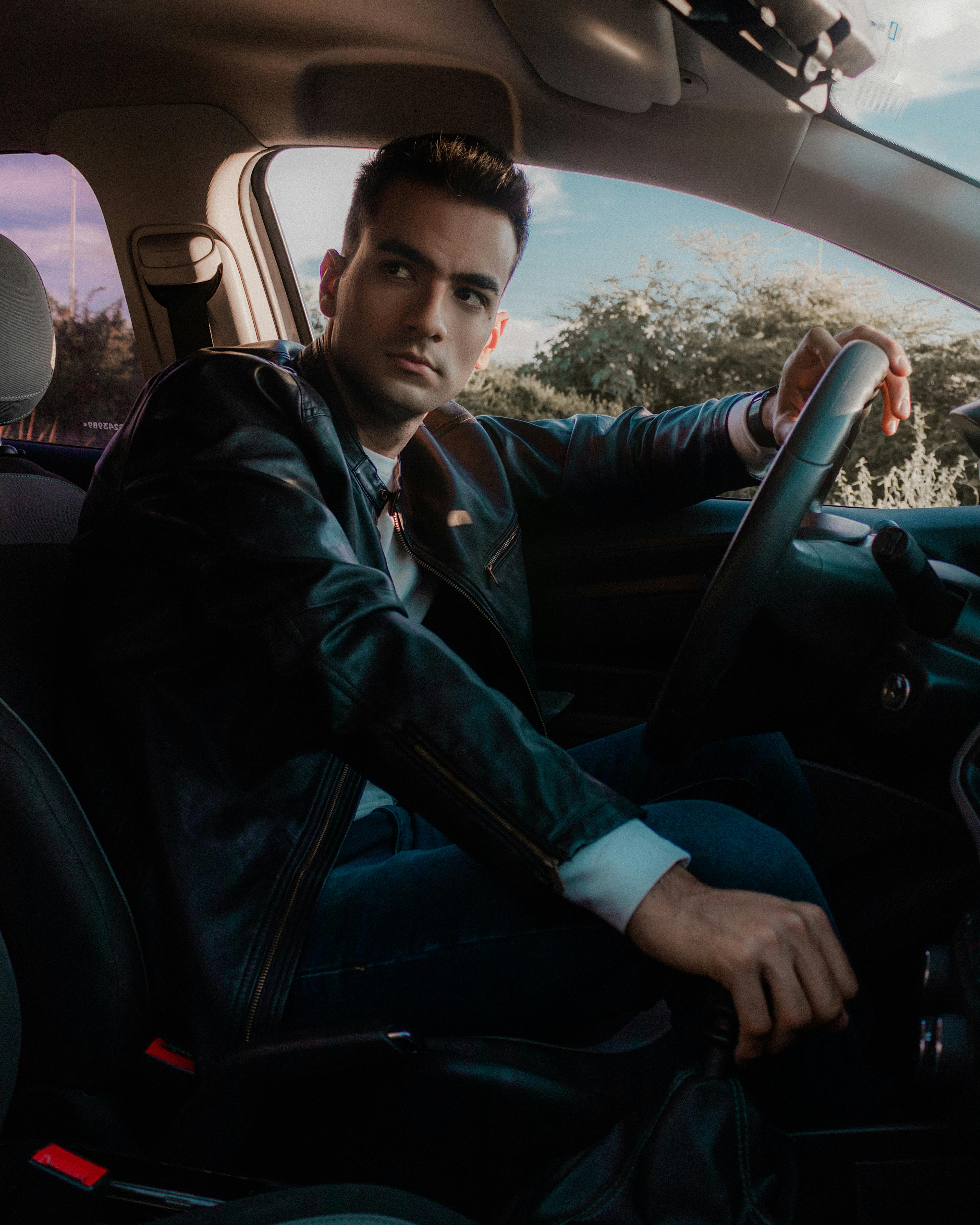 Free Young man in black leather jacket driving a car with focus on interior details. Stock Photo