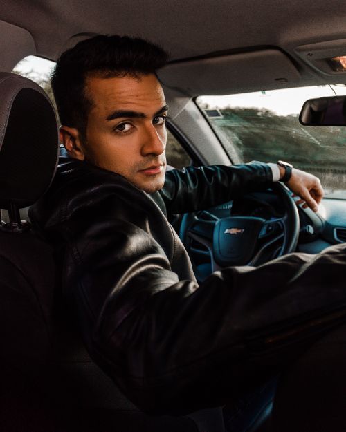 Free A young man in a black leather jacket driving and looking back in a car interior. Stock Photo