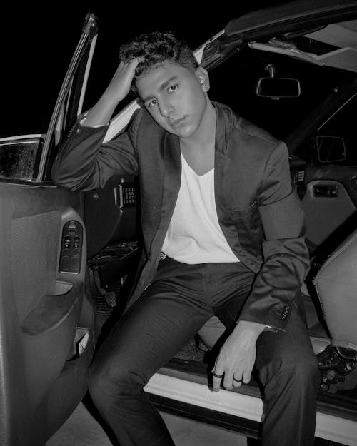 Black and White Shot of a Man in a Suit Jacket Sitting in the Open Car Door
