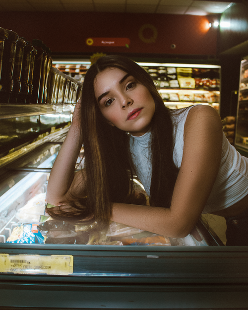 Free Stylish young woman posing confidently in a supermarket, leaning on a freezer Stock Photo