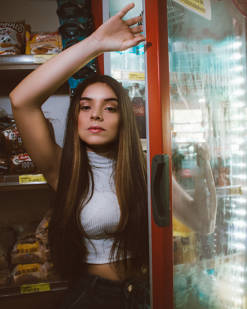 Free Young woman standing at supermarket refrigerator, casual and relaxed pose. Stock Photo