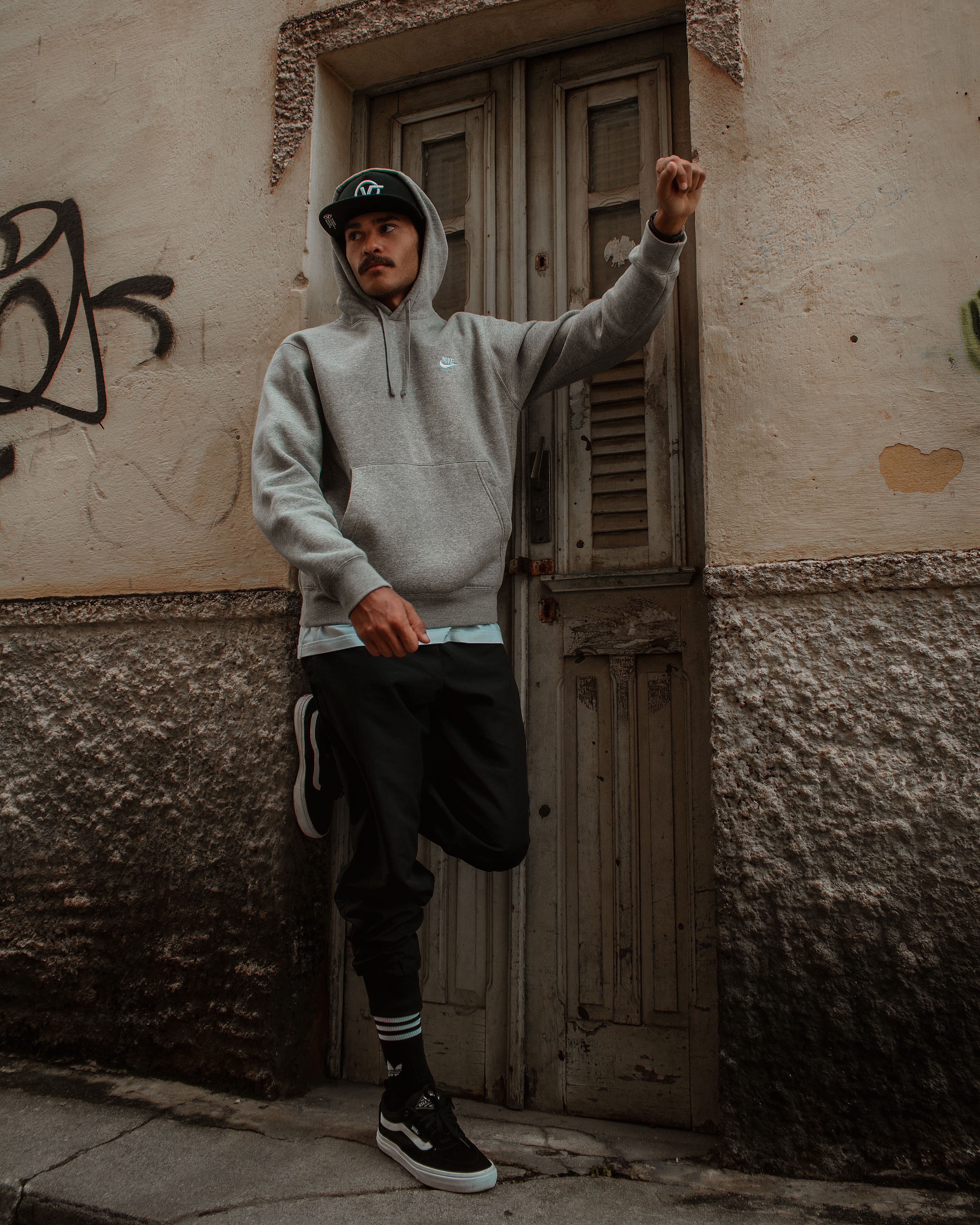 Stylish man in a hoodie posing against a textured door in an urban setting.