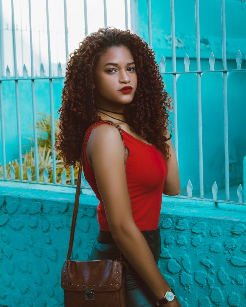 Free A fashionable woman with curly hair poses in front of a turquoise wall, exuding confidence and style. Stock Photo